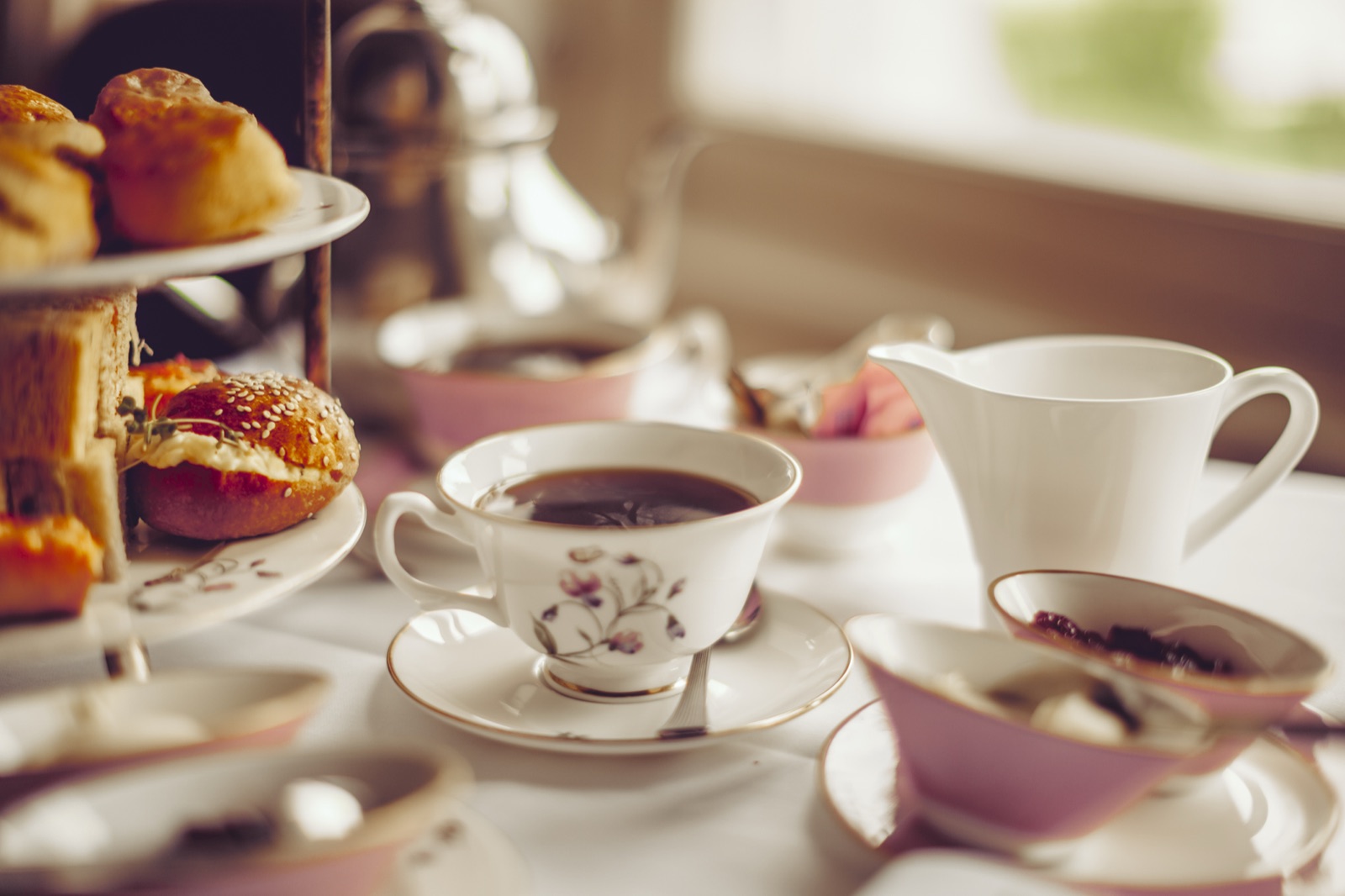 Afternoon tea: a tiered stand of scones, a flowered china cup of tea and a milk jug on a white tablecloth.