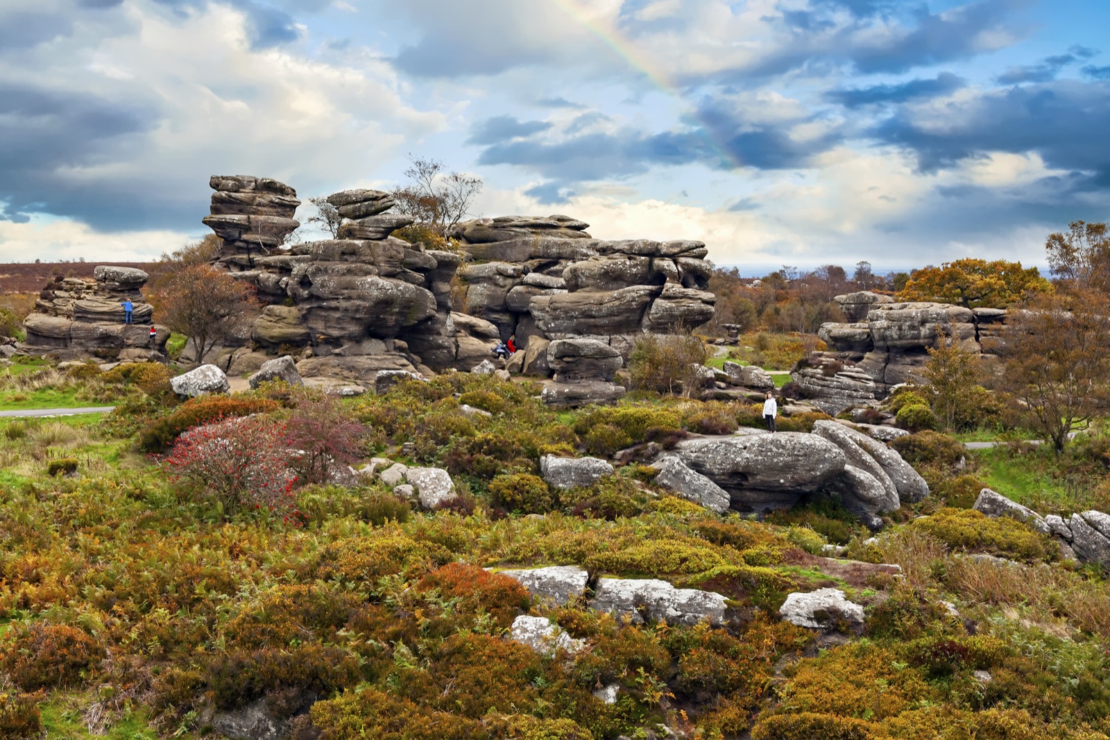 Brimham Rocks: stacks of weathered gritstone on a moorland of autumn heather and bracken, under a cloudy sky with a faint rainbow.
