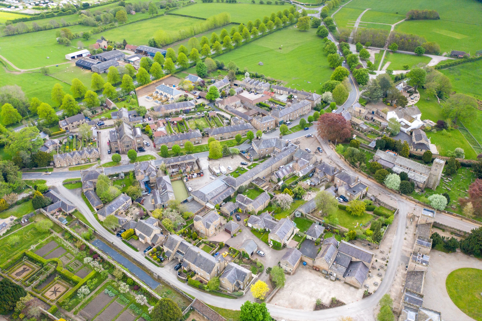 Ripley village from above: stone houses and gardens along curving lanes, surrounded by green fields and tree-lined avenues.