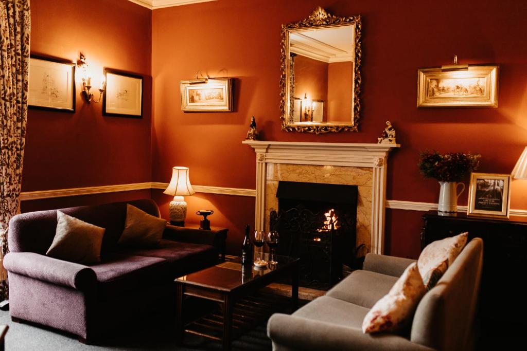 A deep red sitting room with a lit fire, a gilt mirror over the mantelpiece, sofas and lamplight.